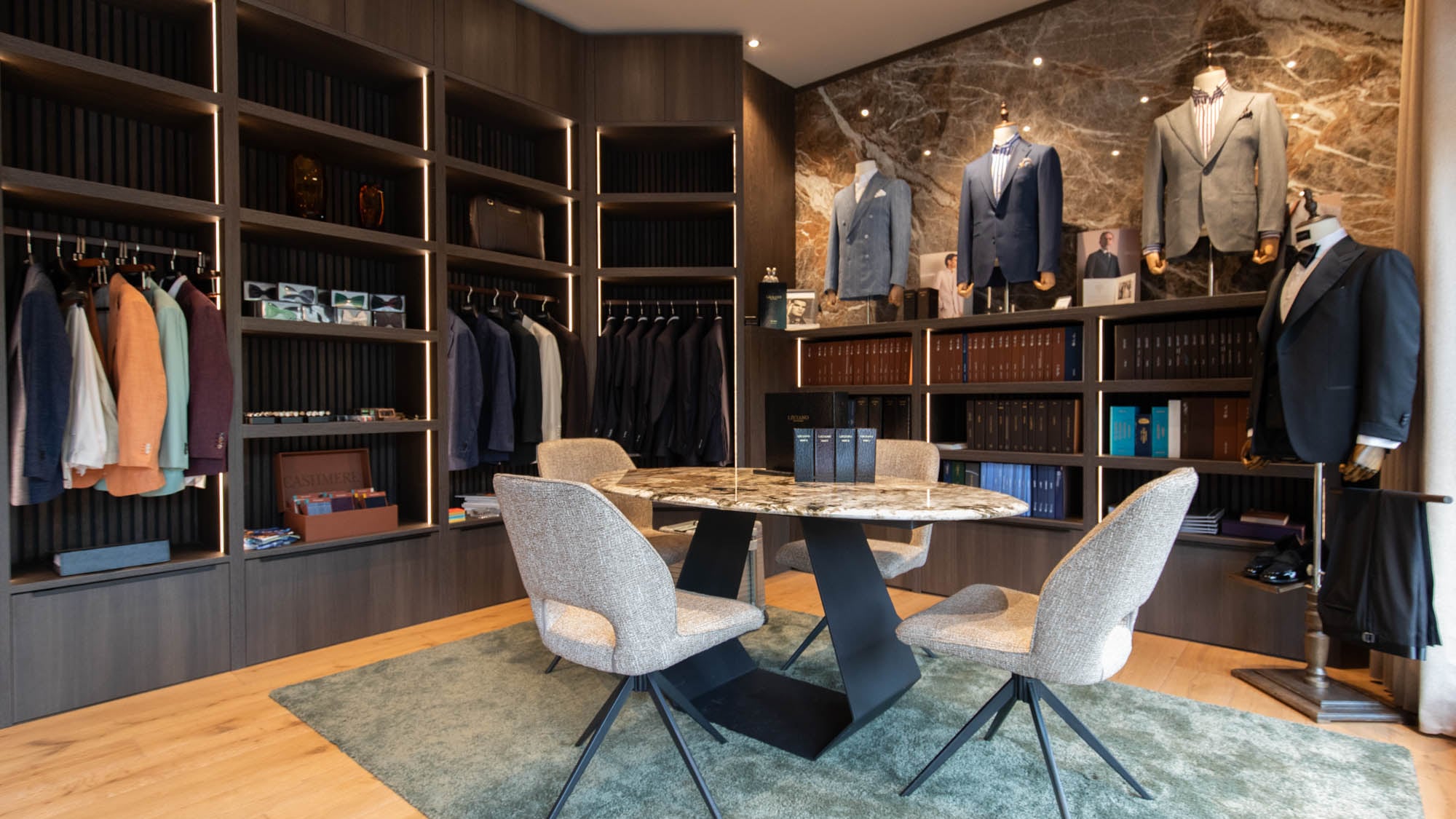 Verkaufsraum des LECIANO Showrooms – Beratungstisch, Regale mit Stoffbüchern und Sakkos vor der Marmorwand