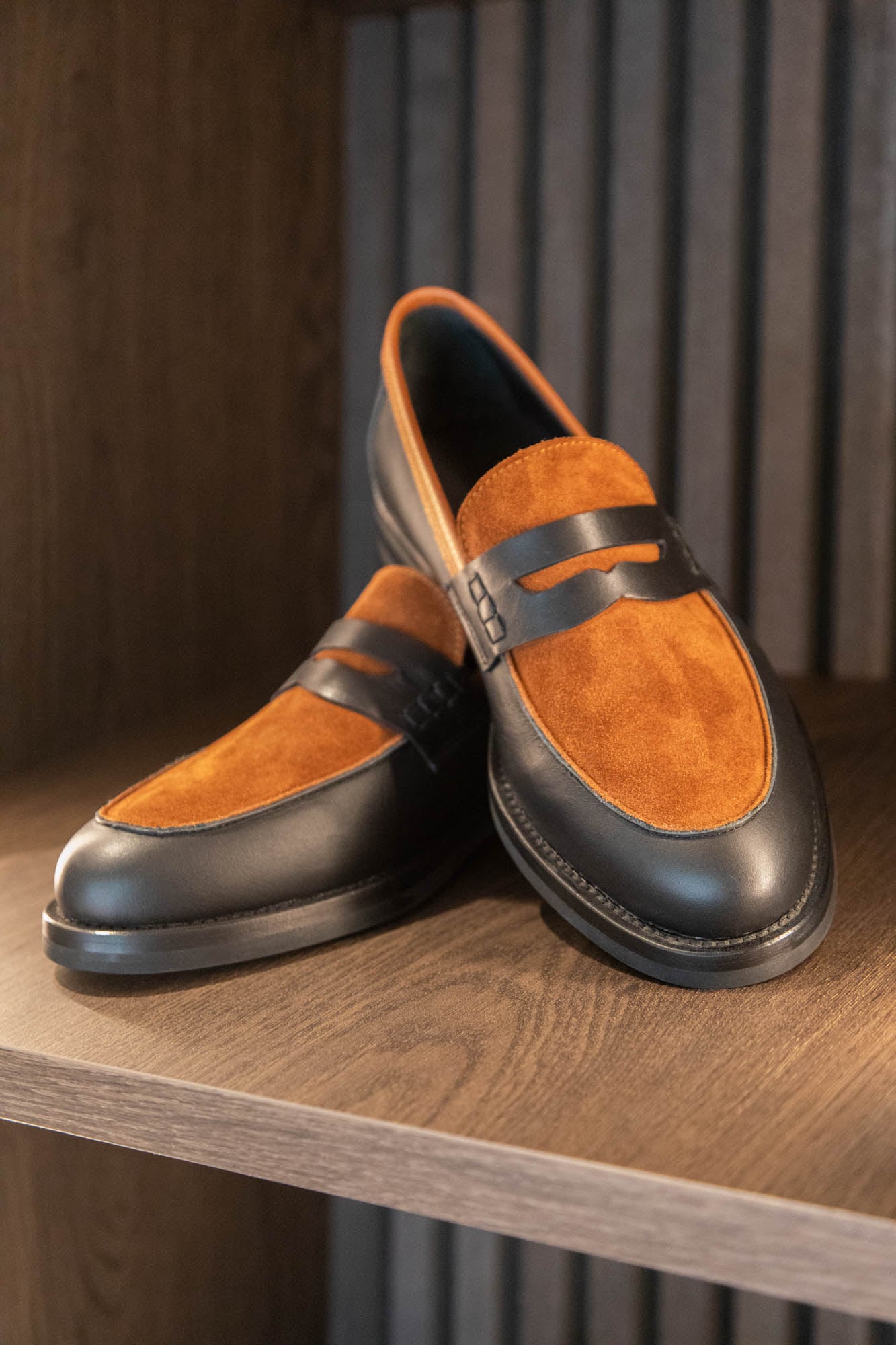 Zweifarbiger Loafer aus schwarzem Glattleder und cognacfarbenem Wildleder im Schuhregal des LECIANO Showrooms