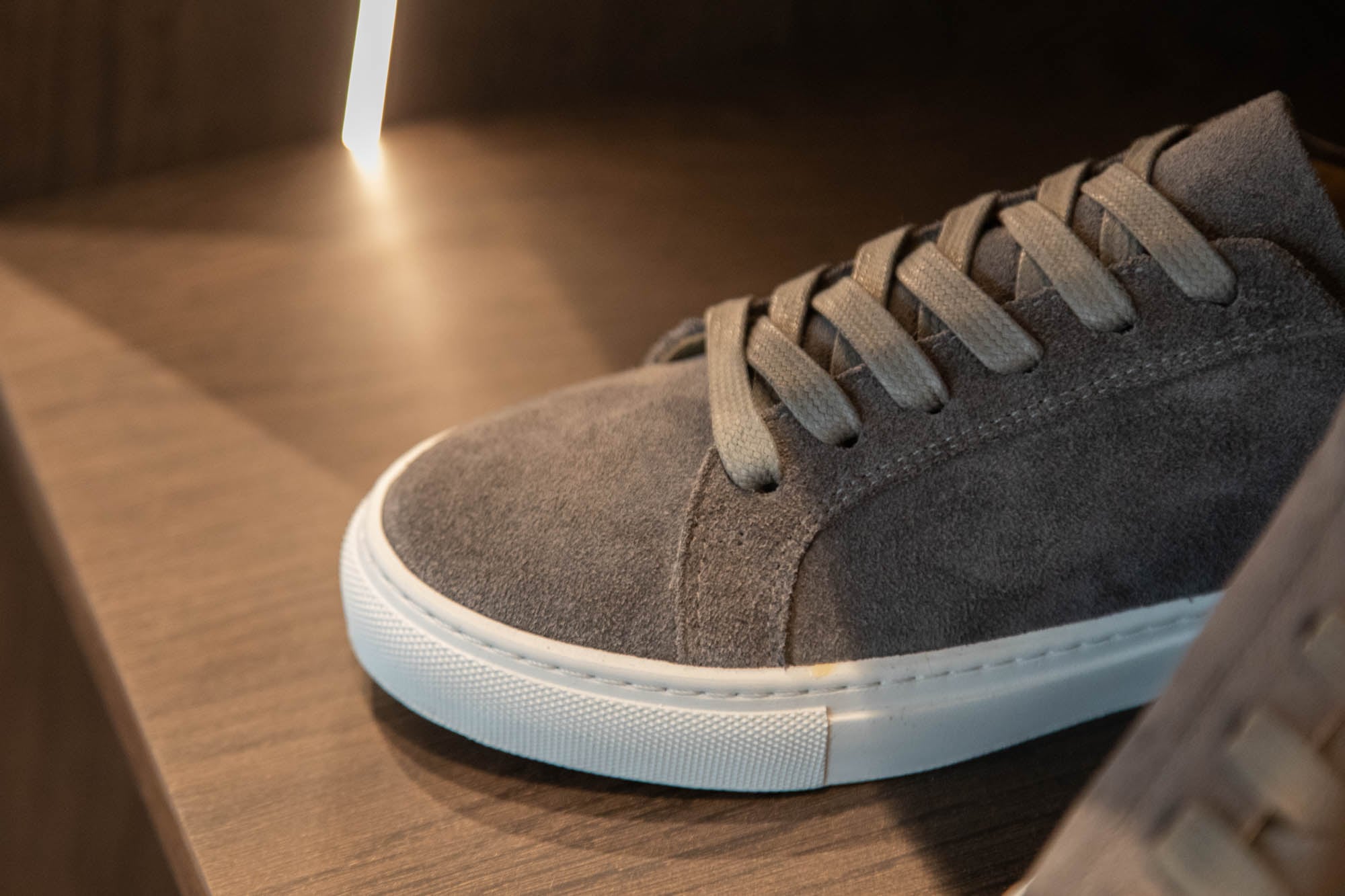 Sneaker aus grauem Wildleder mit weisser Sohle, Detailaufnahme im Schuhregal